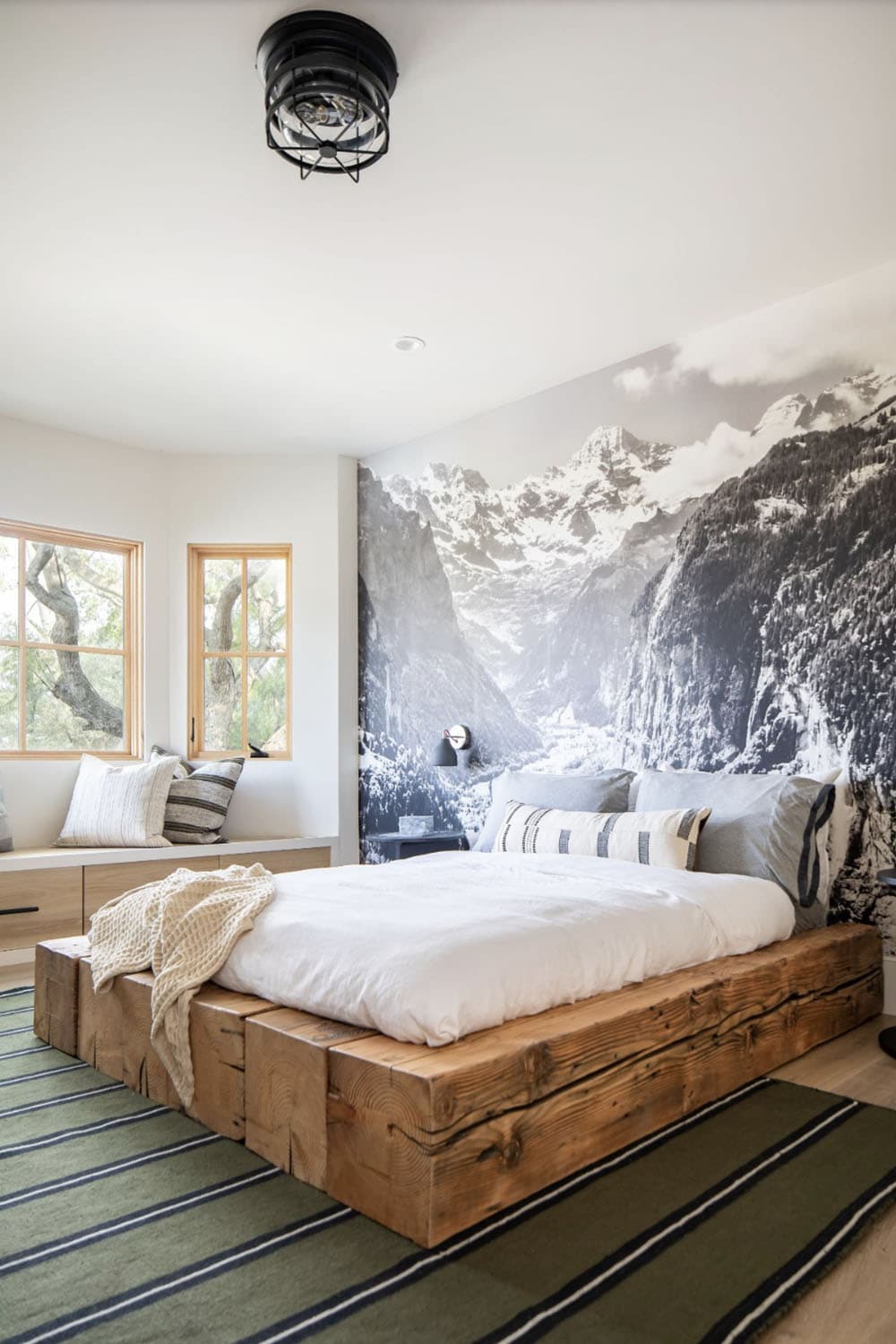 Boy's bedroom with rustic wood platform bed, mountain mural wallpaper, window seat, and black cage ceiling light