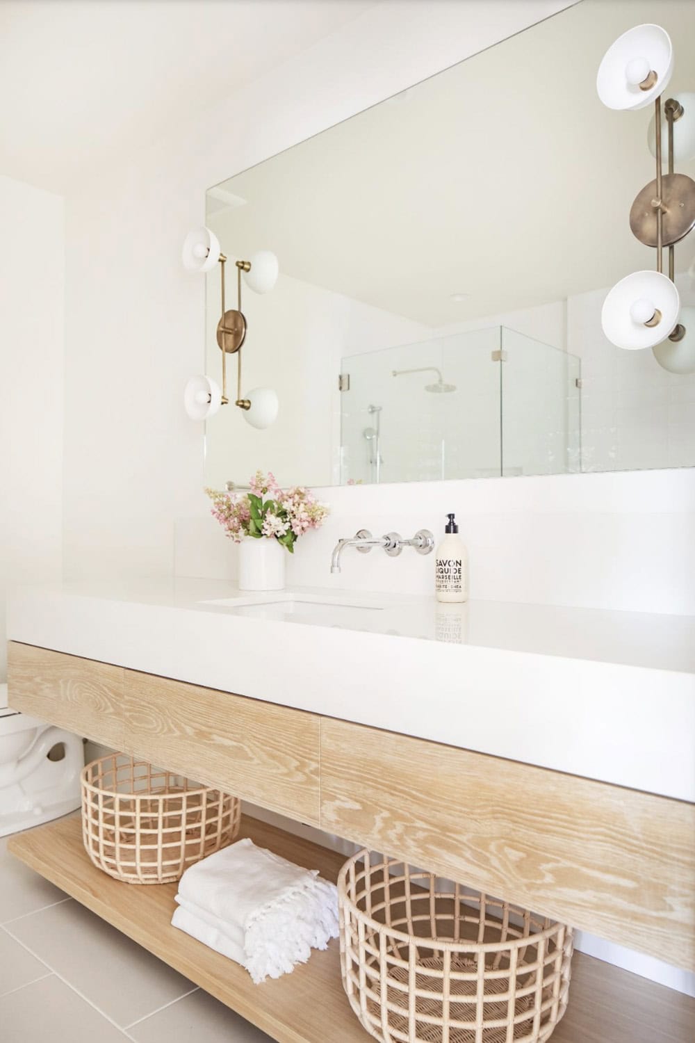 Bathroom vanity with floating oak cabinet, white trough sink, full-width mirror, and brass globe sconces