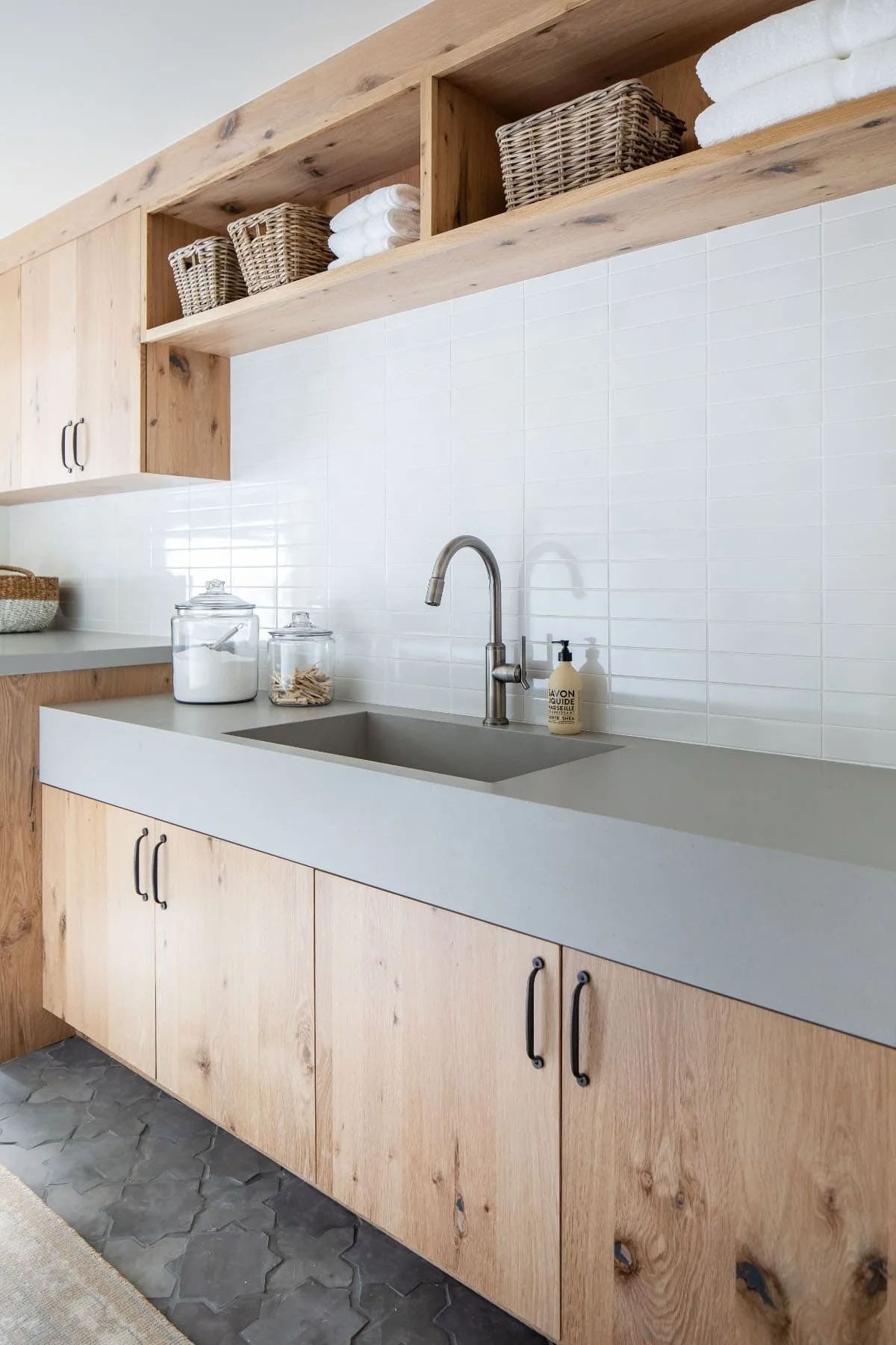 Laundry room with knotty oak cabinets, gray concrete countertop, white subway tile backsplash, and hexagon floor tile