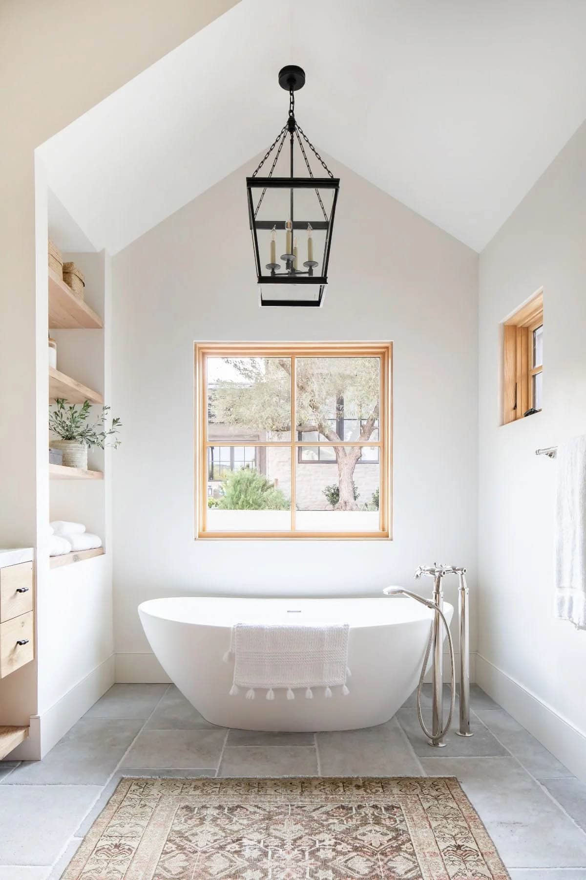 Primary bathroom with freestanding soaking tub, vaulted ceiling, black lantern pendant, and garden view window