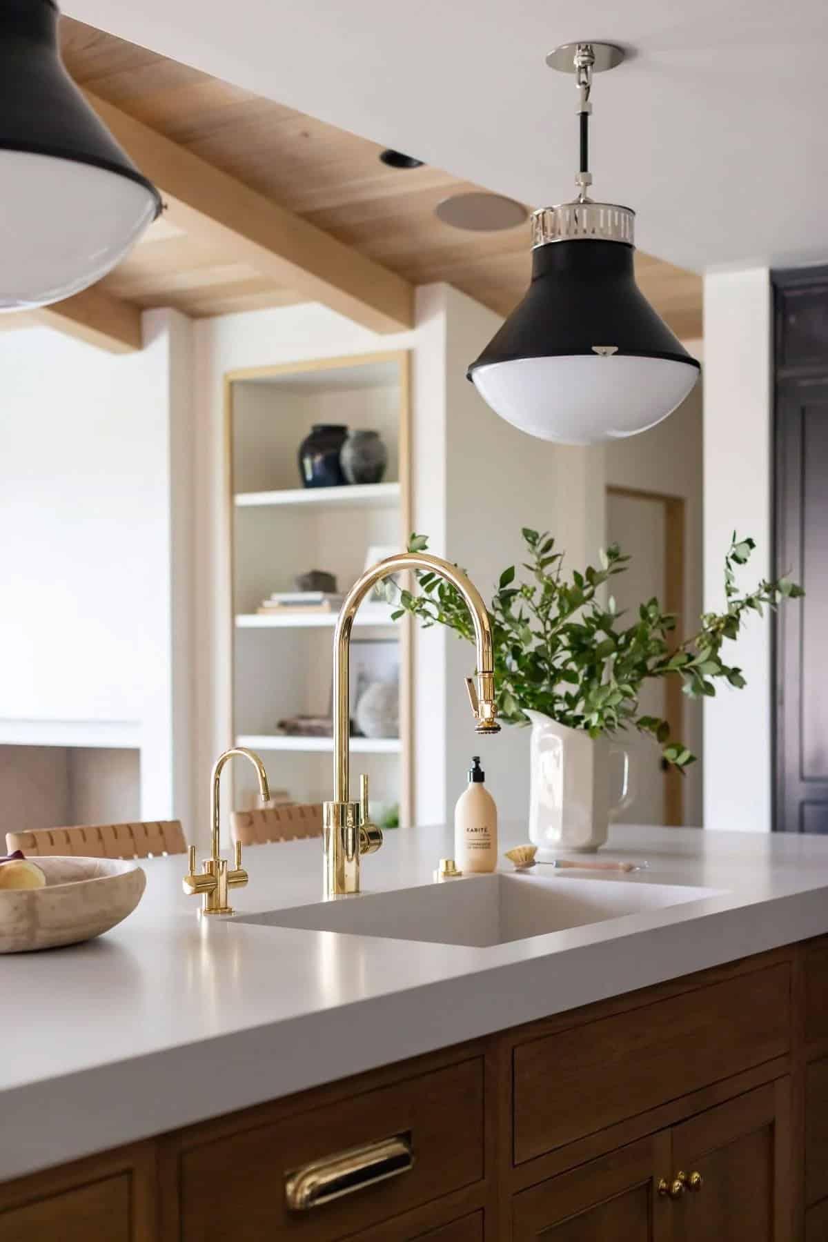 kitchen island, brass faucet, white quartz countertop, black pendant lights, wood beam ceiling