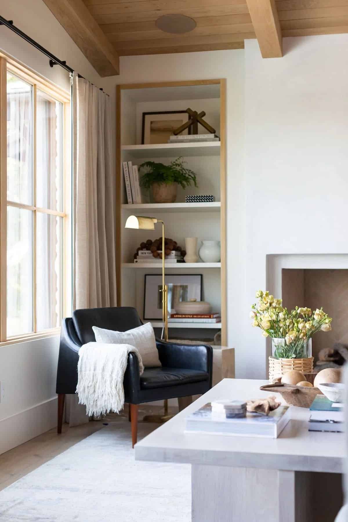 living room, black leather chair, built-in bookcase, plaster fireplace, wood beam ceiling, brass floor lamp