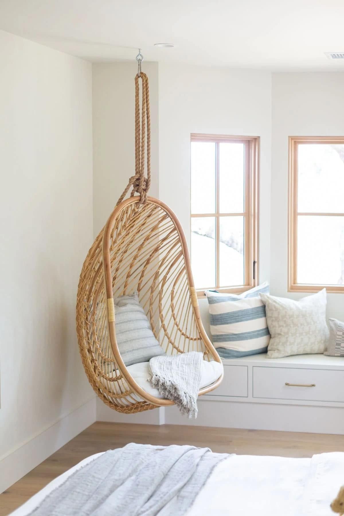 bedroom, hanging rattan chair, built-in window seat with storage, coastal pillows, natural wood windows