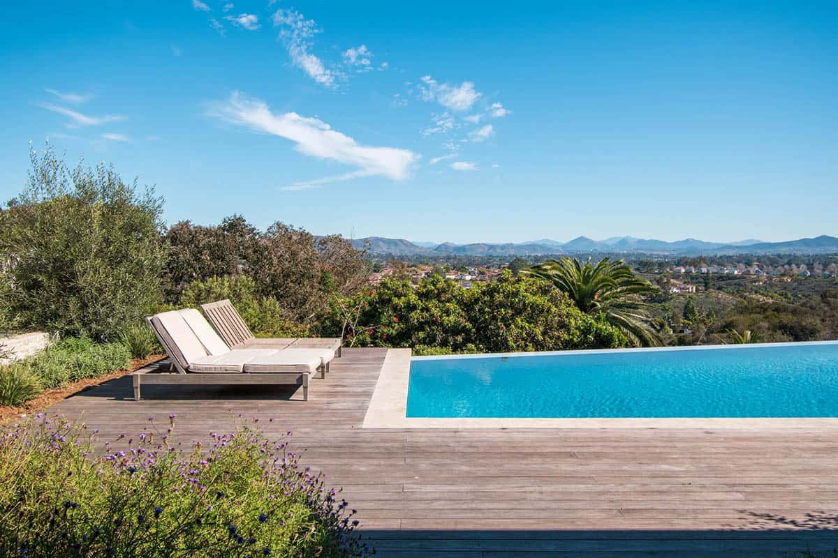 Infinity pool with lounge chairs overlooking a scenic valley and distant mountains