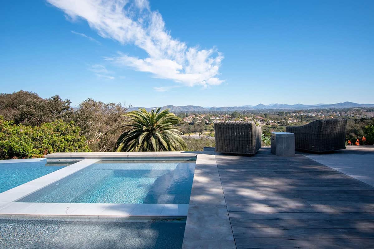Modern infinity pool and hot tub on a patio overlooking a valley with palm trees and distant hills