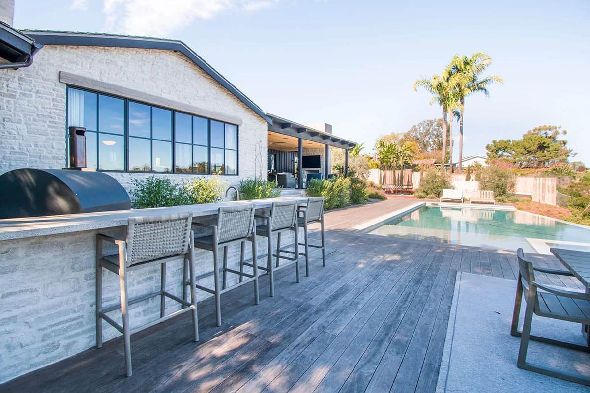 Backyard with a modern pool, wooden deck, and outdoor bar beside a contemporary home