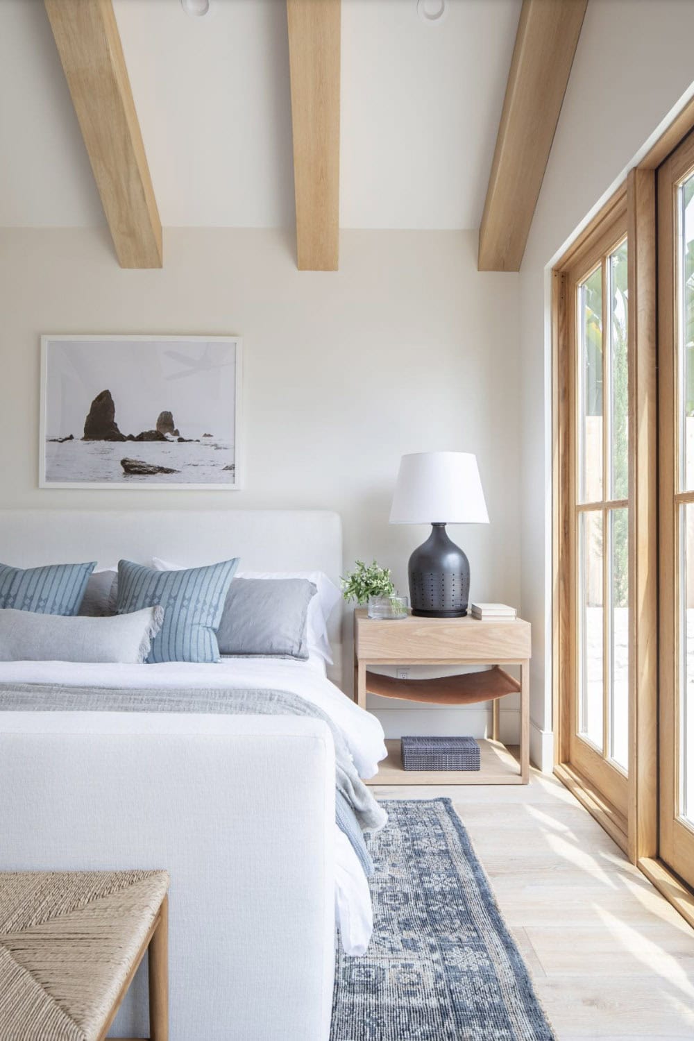 Primary bedroom with wood beam vaulted ceiling, white upholstered bed, and French doors opening to garden