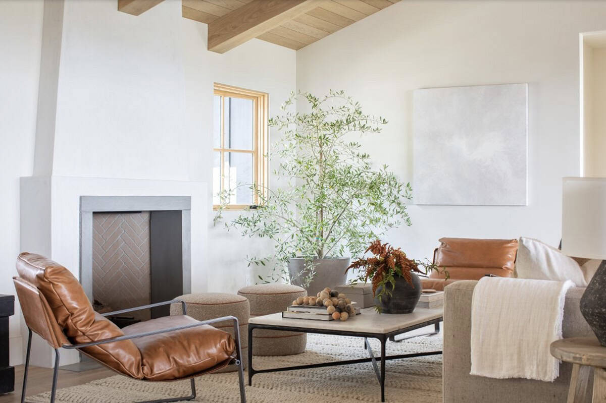 Living room corner with wood beam ceiling, leather chair, stone fireplace, ottomans, and large potted olive tree