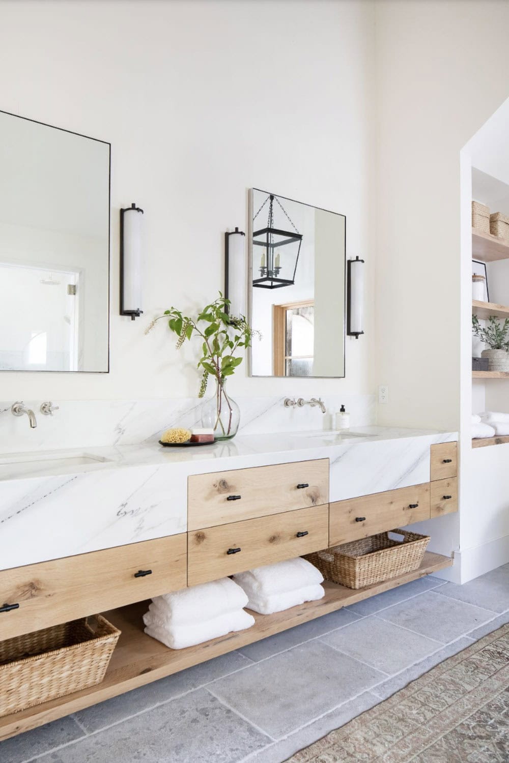 Primary bathroom double vanity with floating oak cabinet, white marble countertop, and black-framed mirrors