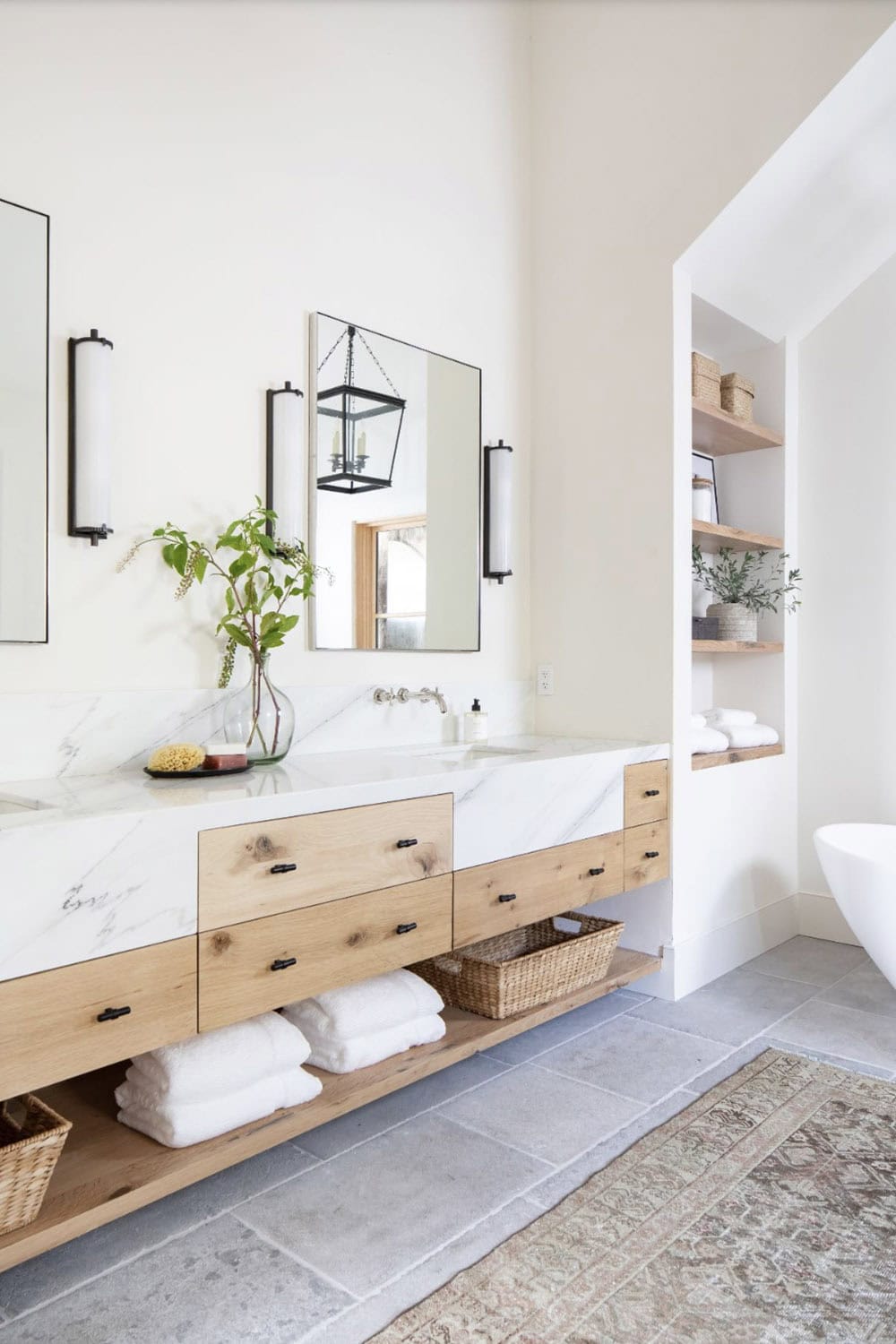 Primary bathroom double vanity with floating oak cabinet, white marble countertop, and black-framed mirrors