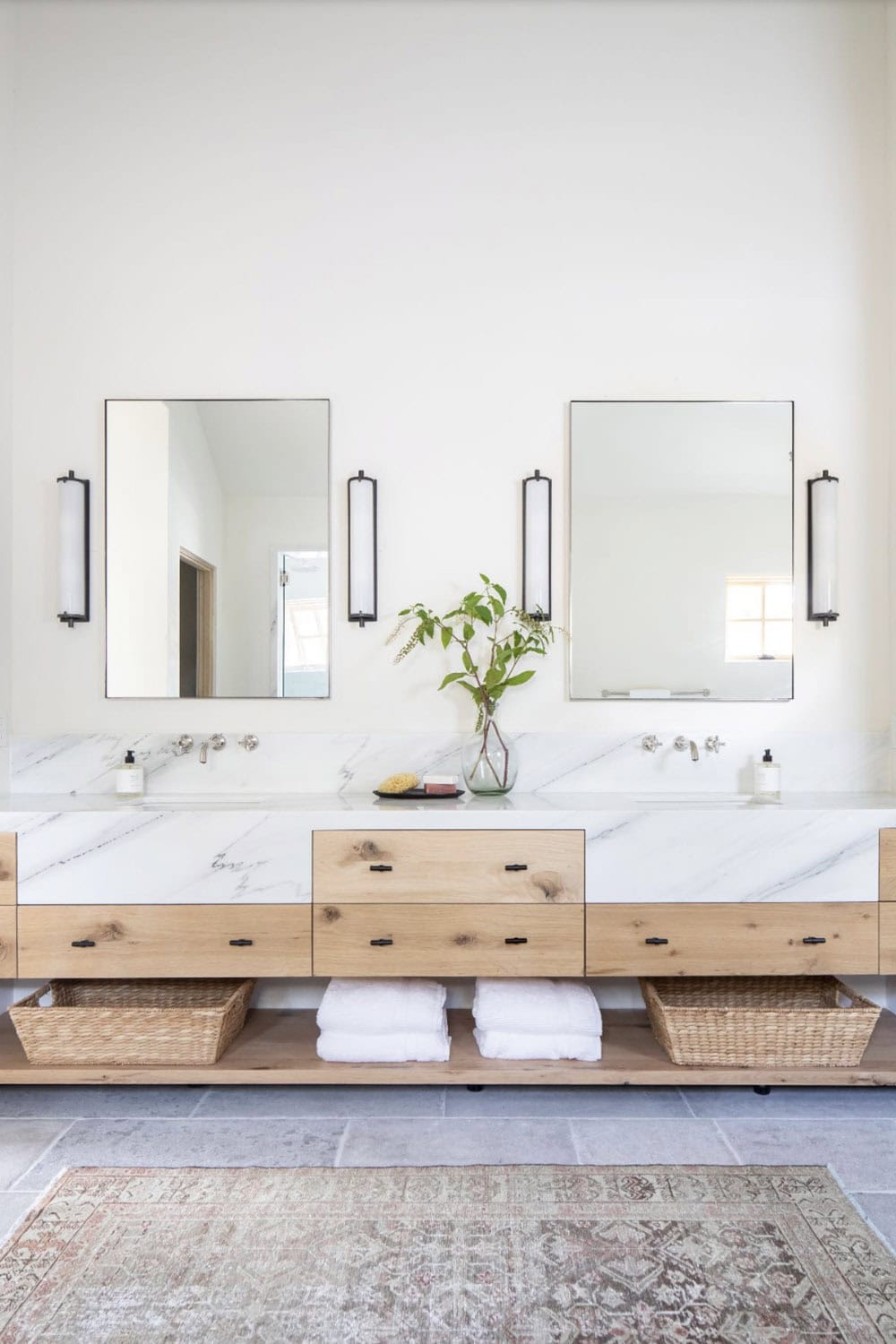 Primary bathroom double vanity with floating oak cabinet, white marble countertop, and black-framed mirrors