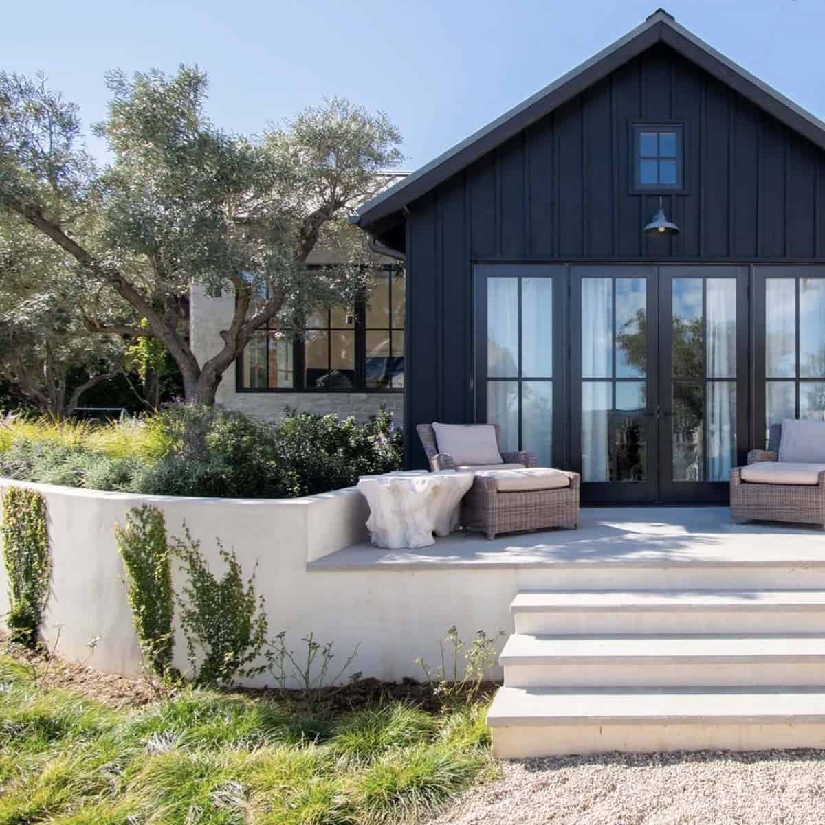 Rear exterior of a dark board-and-batten guest house with French doors, concrete patio, and wicker seating