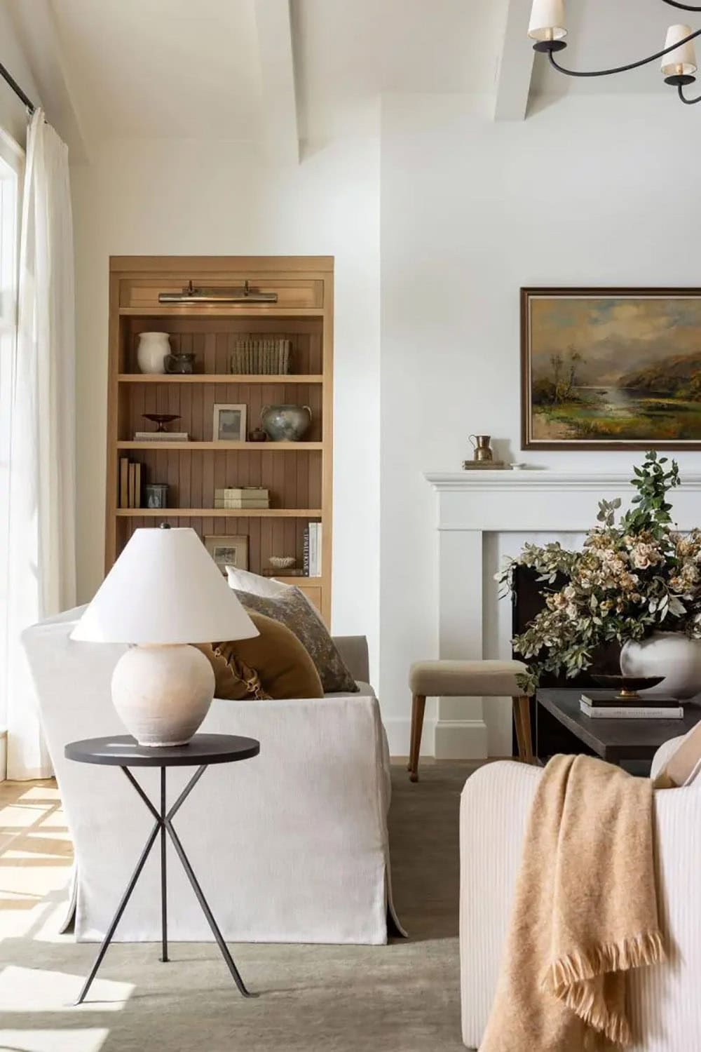 Close-up of oak built-in bookshelf with brass picture light, vintage landscape painting above white fireplace
