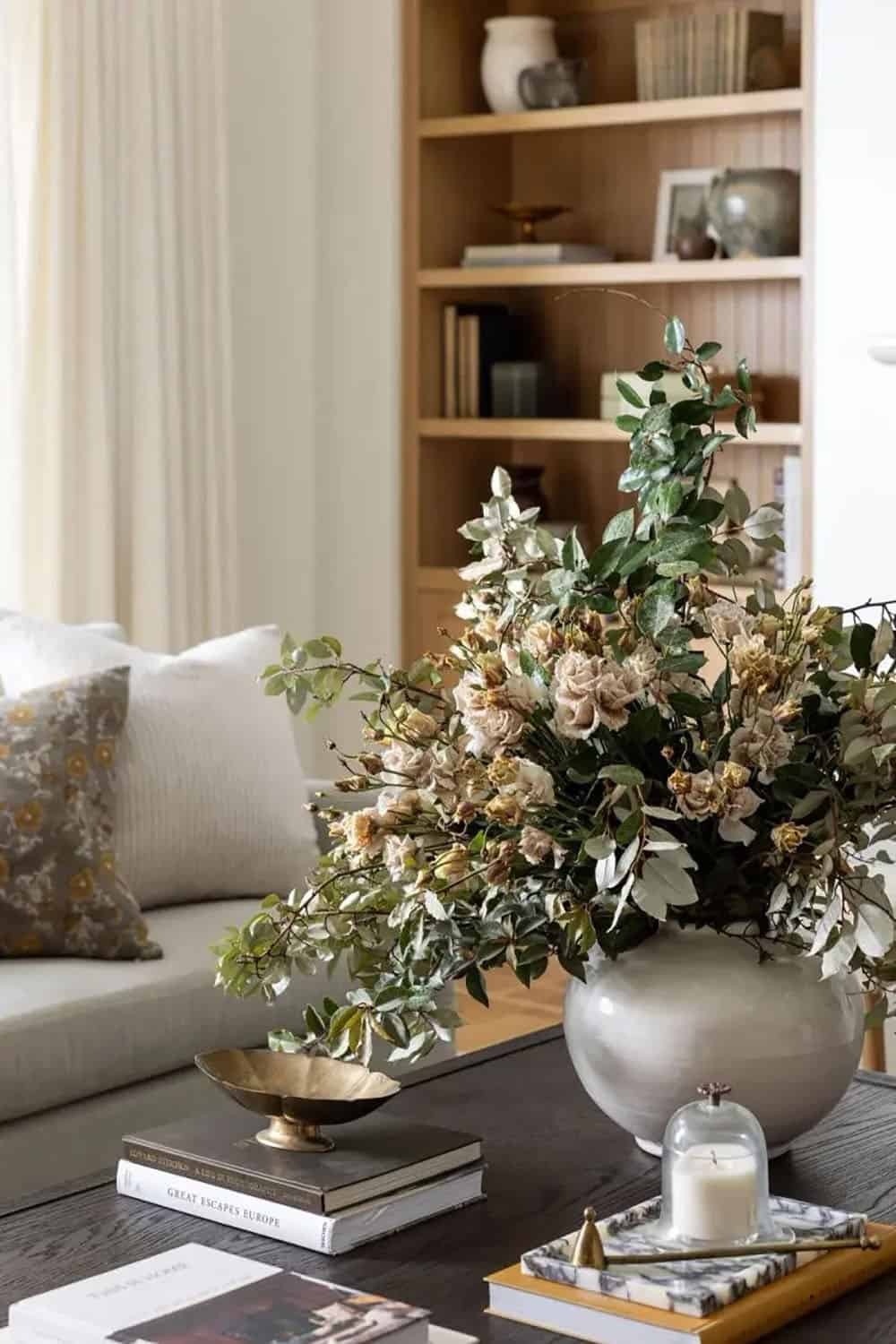 Close-up of floral centerpiece in silver vase on dark wood coffee table with styled books and brass dish