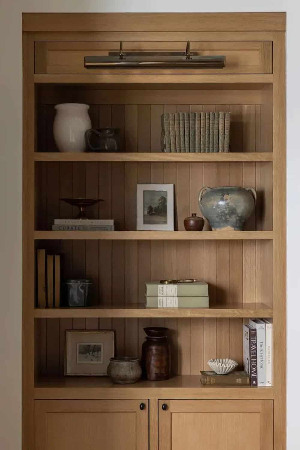 Close-up of styled oak built-in bookshelf with brass picture light, pottery, vintage books, and framed art