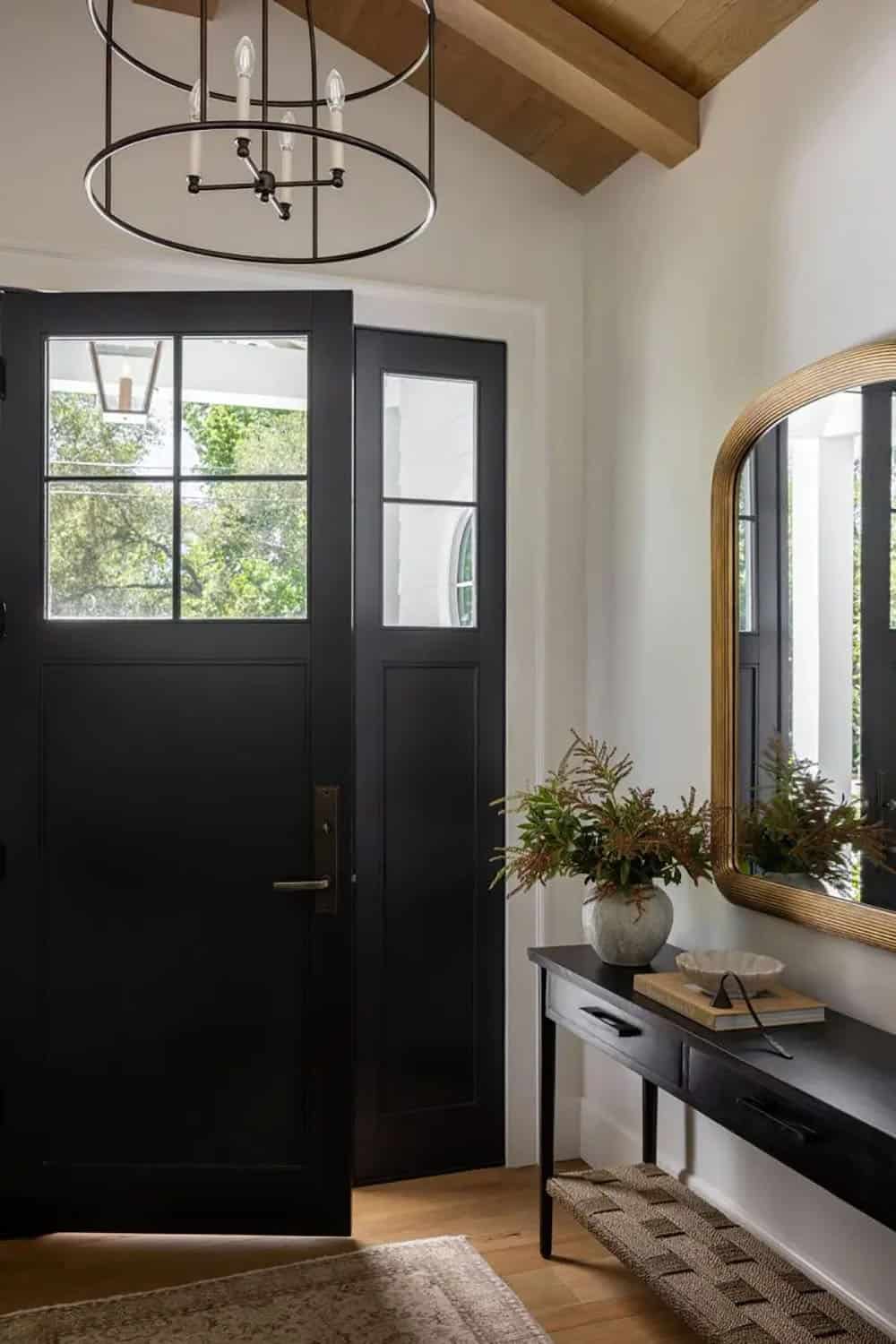 Entryway with black double front door, iron ring chandelier, black console table, and gold arched mirror