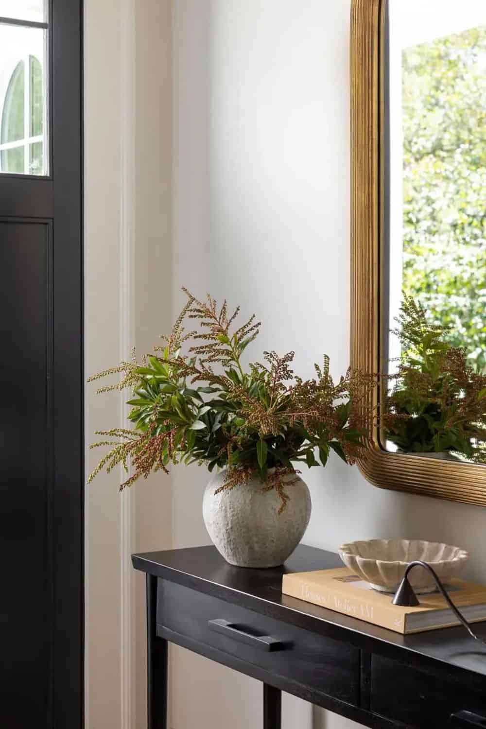 Close-up of black console table styled with textured vase, greenery arrangement, and gold arched mirror