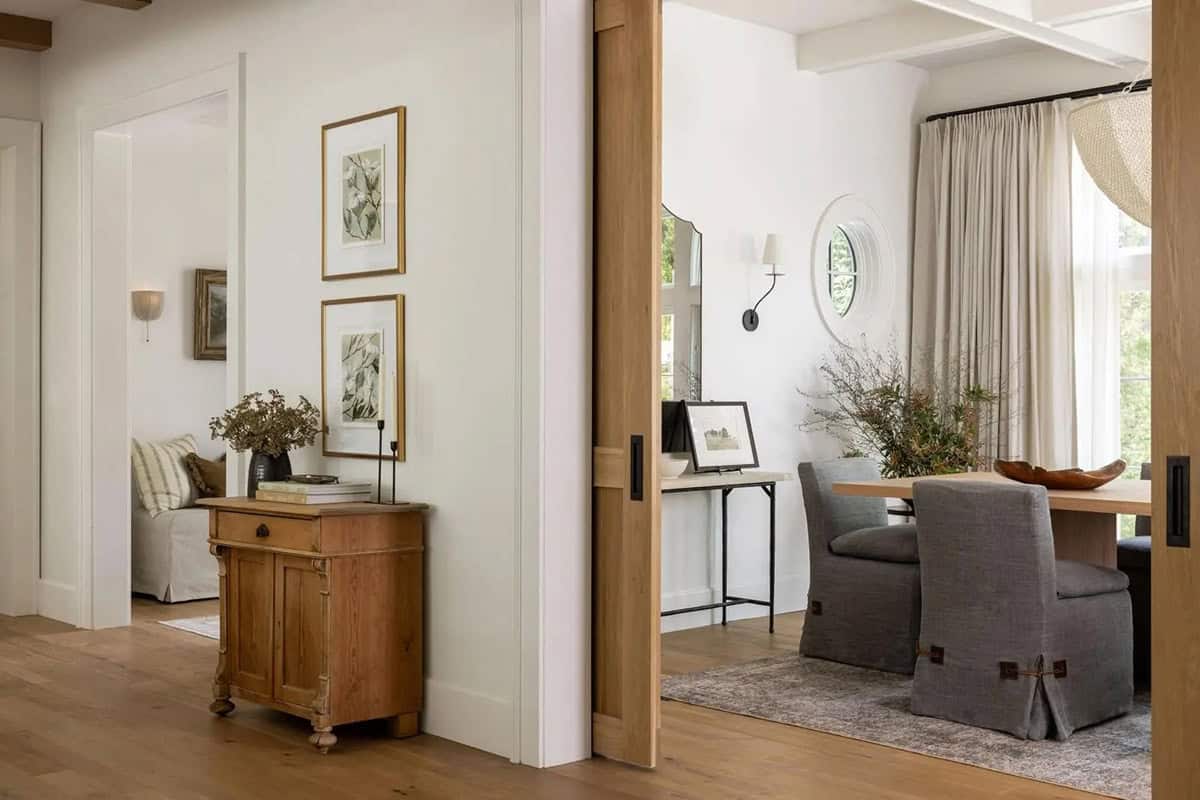 Hallway view into dining room through oak pocket doors with antique chest and botanical art prints