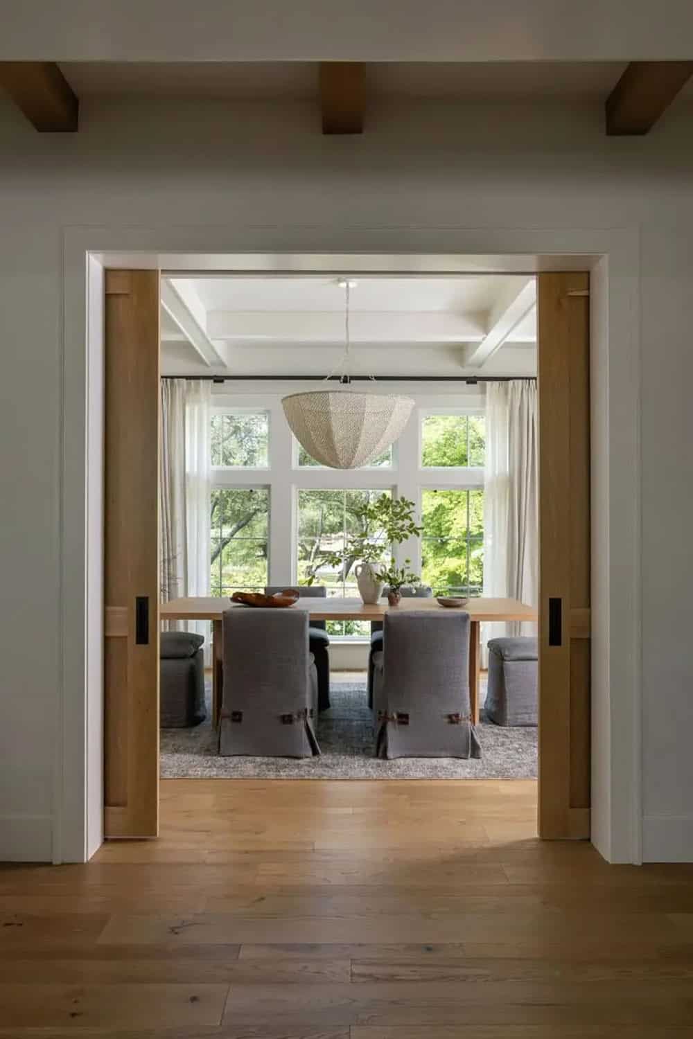 Dining room framed by oak pocket doors with gray slipcovered chairs, oak table, and woven pendant light
