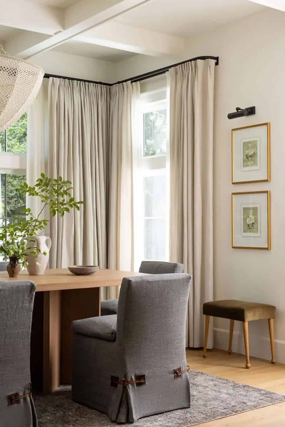 Dining room corner with gray slipcovered chairs, linen drapes, and gold-framed botanical prints