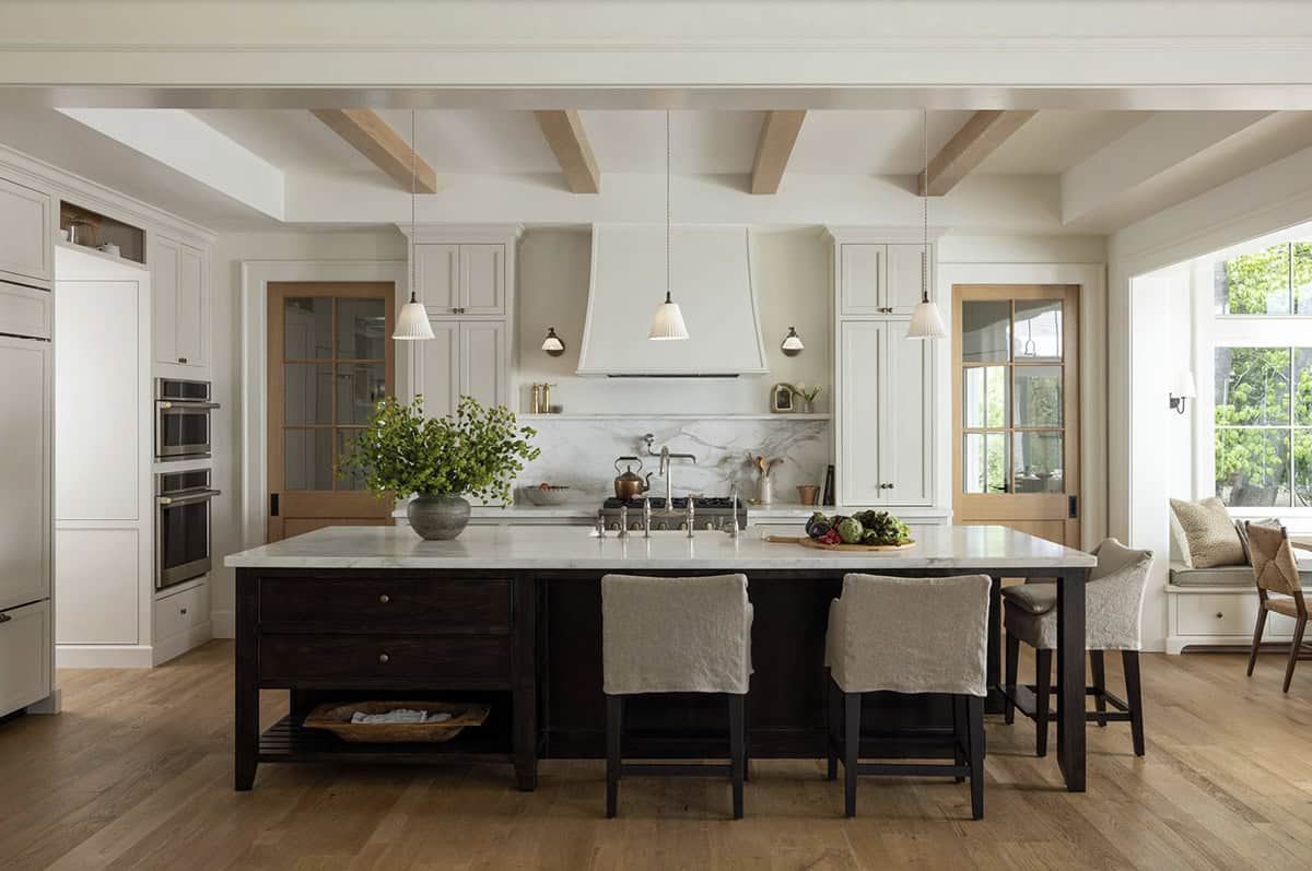 Traditional kitchen with white cabinets, dark island, marble countertops, plaster range hood, and oak beams