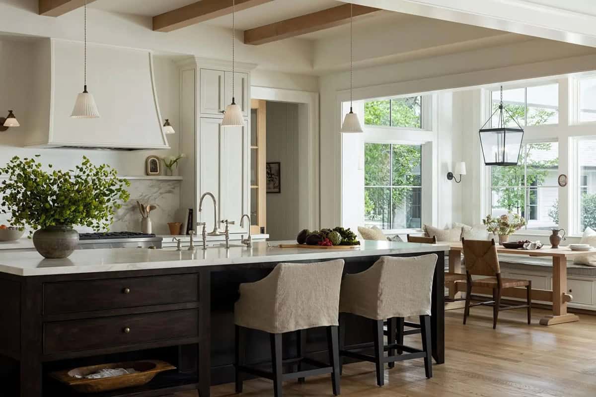 Kitchen with white cabinets, dark island, pleated pendants, and breakfast nook with garden views beyond