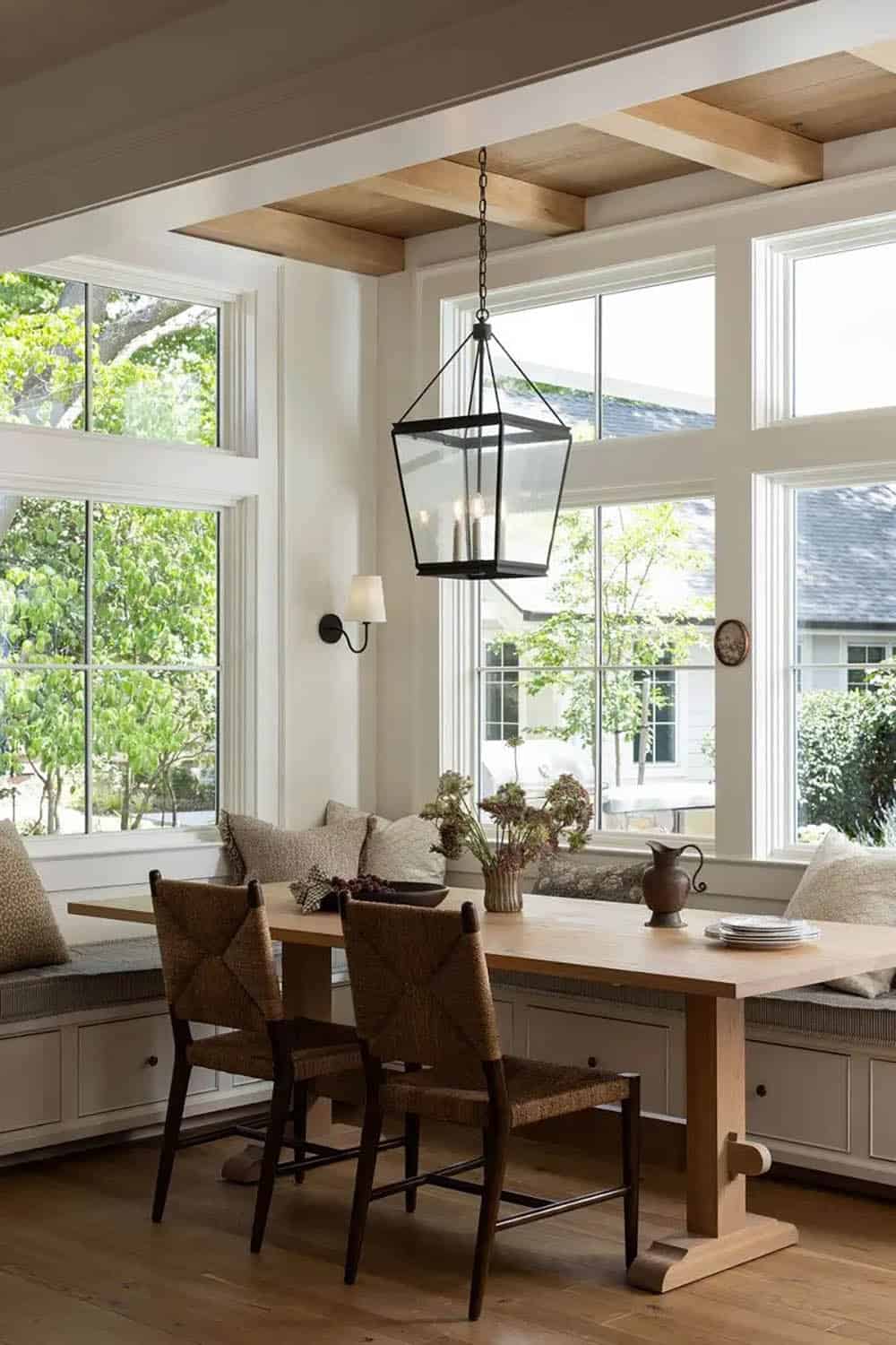 Bright breakfast nook with floor-to-ceiling windows, black lantern pendant, oak table, and window seat banquette