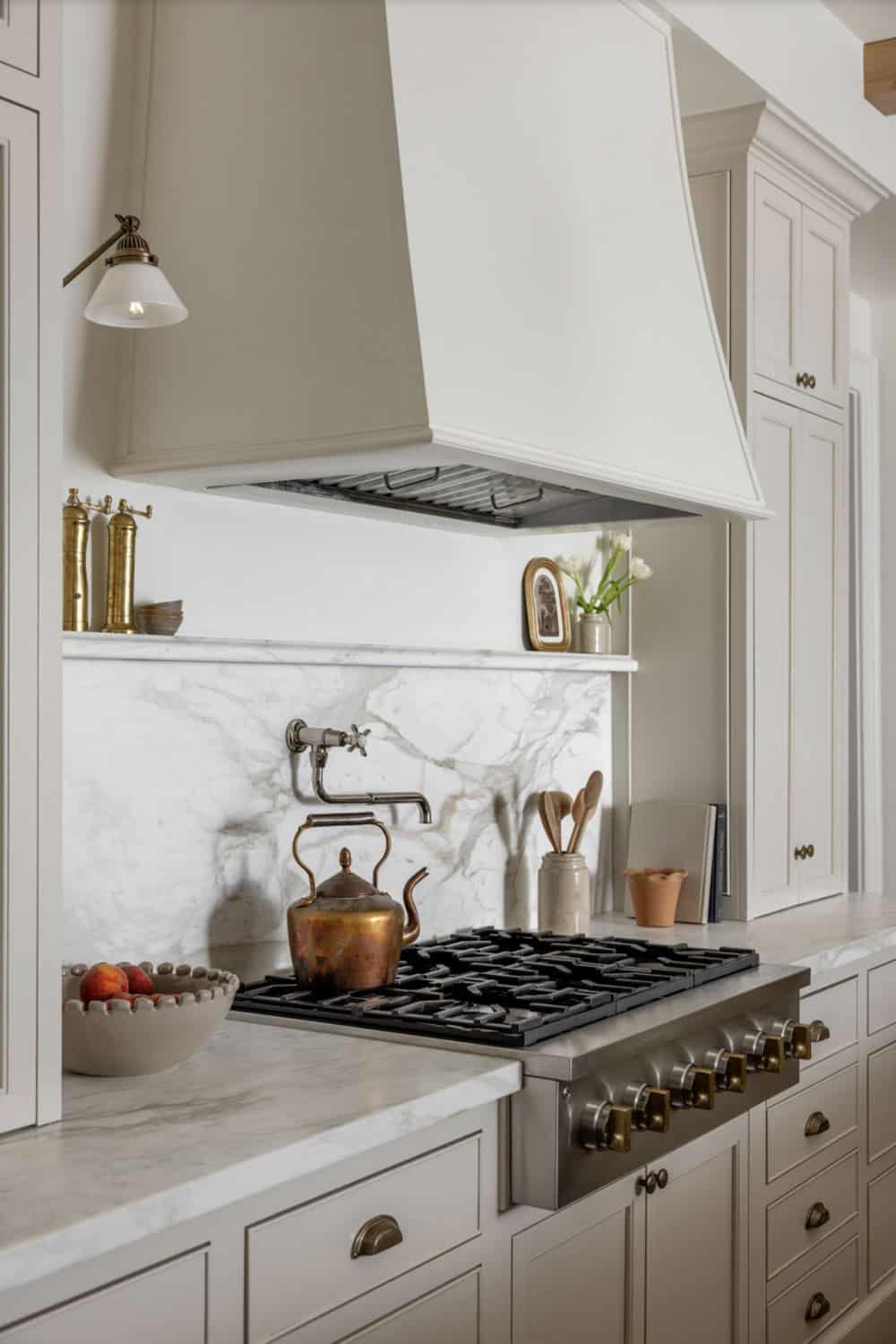 Kitchen range area with plaster range hood, marble slab backsplash, pot filler, and brass hardware