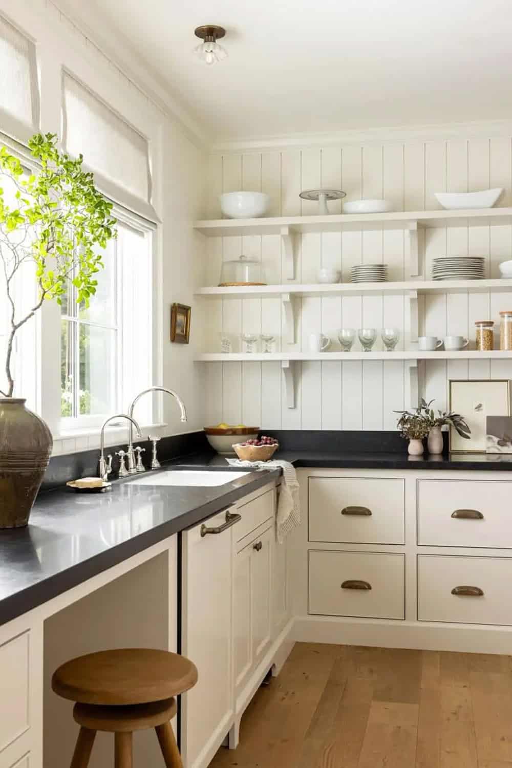 Butler's pantry with cream shaker cabinets, black soapstone countertops, open shelving, and wood stool