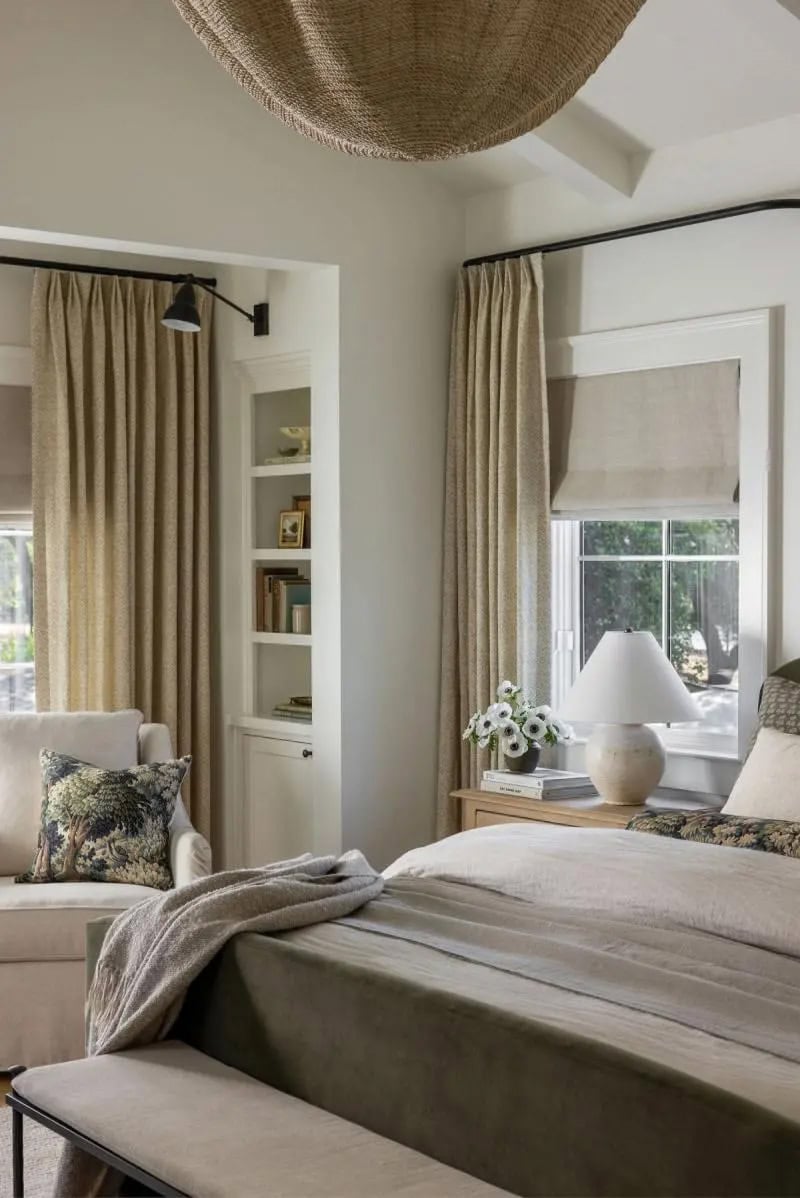 Primary bedroom corner with olive green bed, woven pendant light, linen drapes, and black swing arm sconce