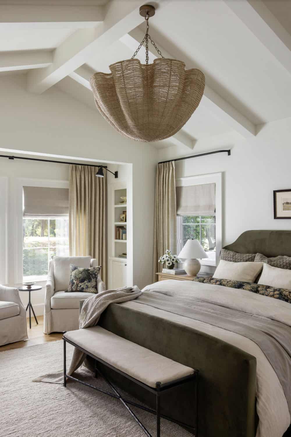 Primary bedroom with vaulted beamed ceiling, large woven pendant, olive green bed, and sitting area