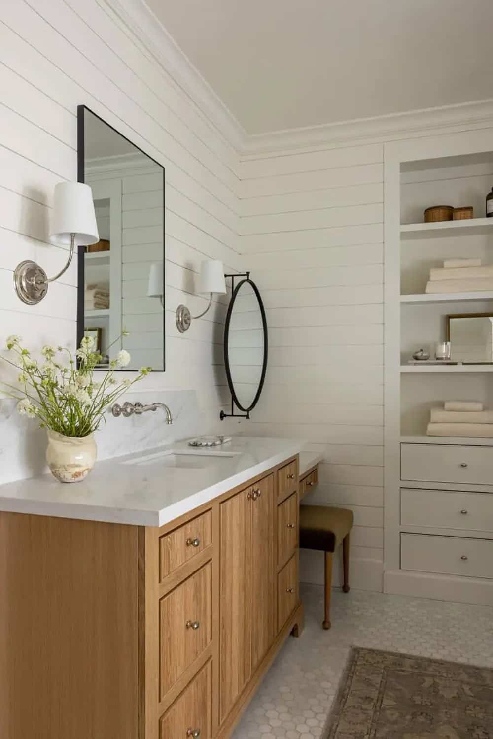 Primary bathroom vanity with oak cabinet, white marble countertop, black-framed mirror, and silver sconces