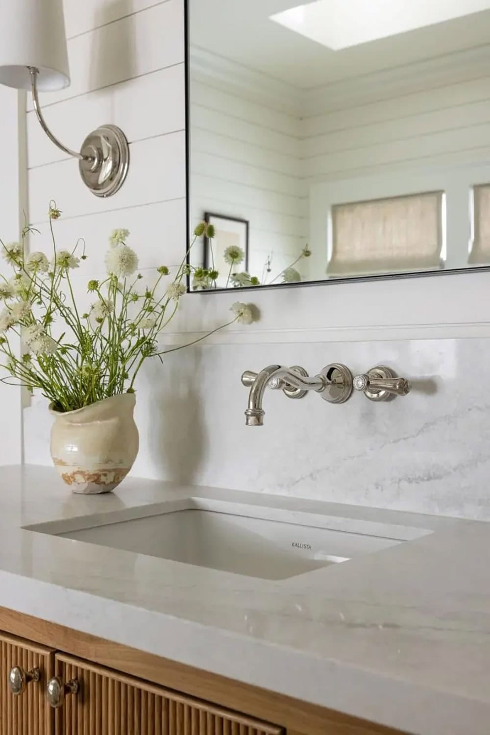 Close-up of bathroom vanity with white marble countertop, wall-mounted nickel faucet, and wildflower arrangement