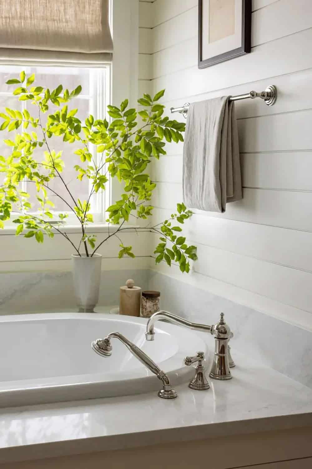 Close-up of soaking tub with polished nickel bridge faucet, shiplap surround, and bright green branch arrangement
