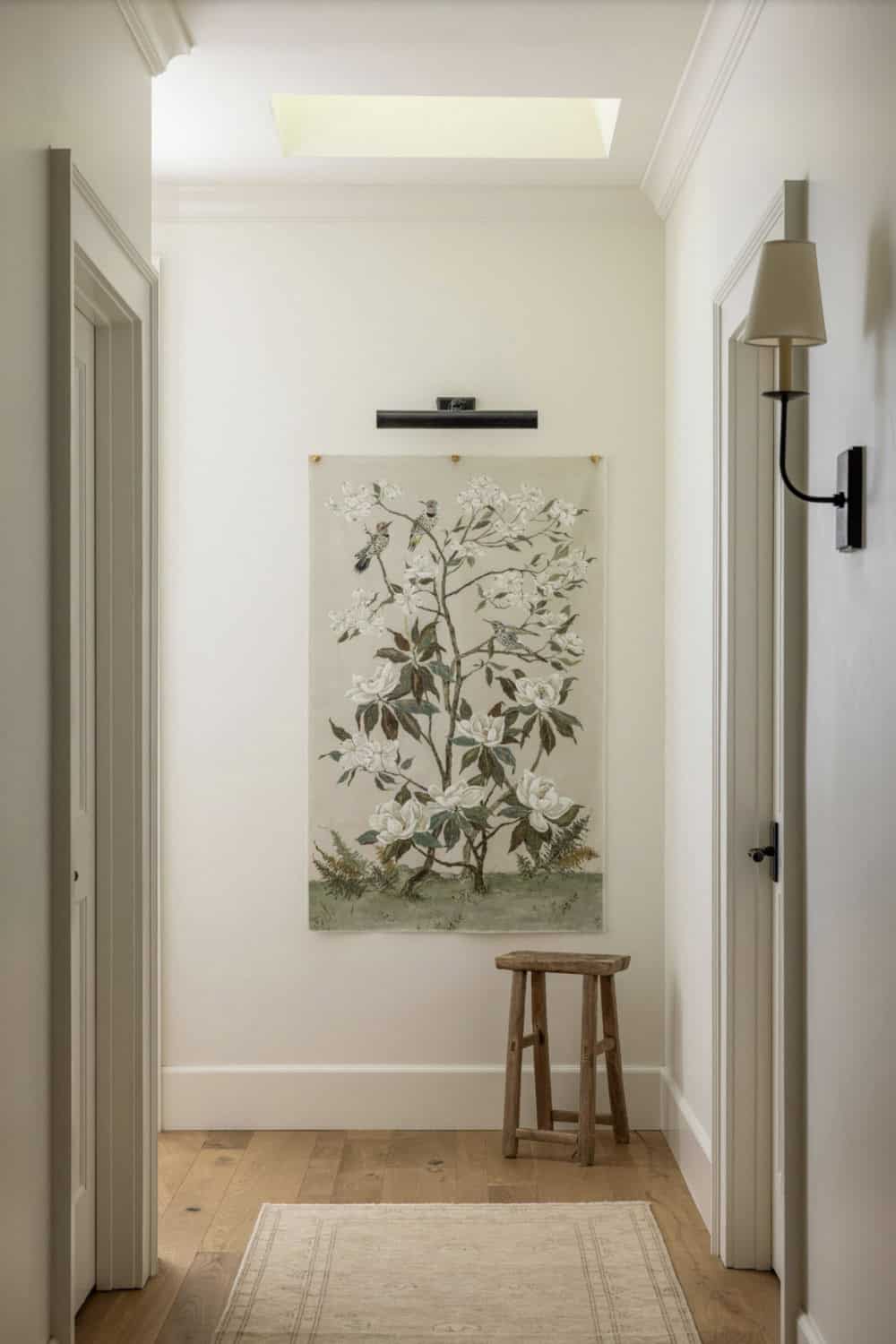 Hallway with botanical tapestry wall art, skylight, and rustic wooden stool