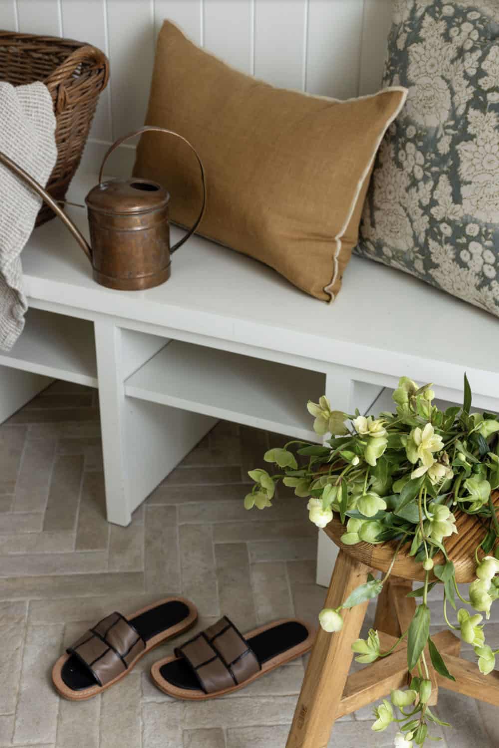 Mudroom bench detail with copper watering can, leather sandals, and green plants