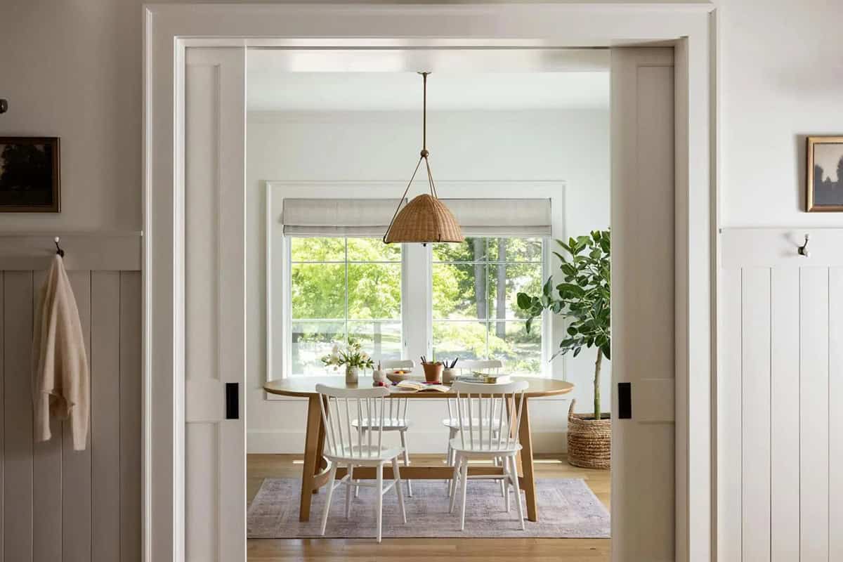 Breakfast nook with round wood table, white Windsor chairs, and wicker pendant light
