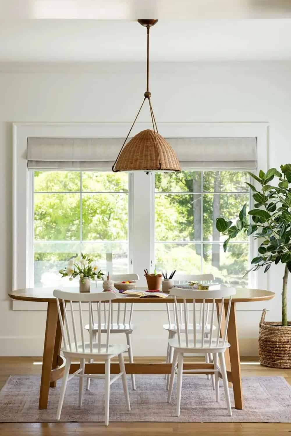Bright dining area with oval wood table, white spindle chairs, and rattan pendant