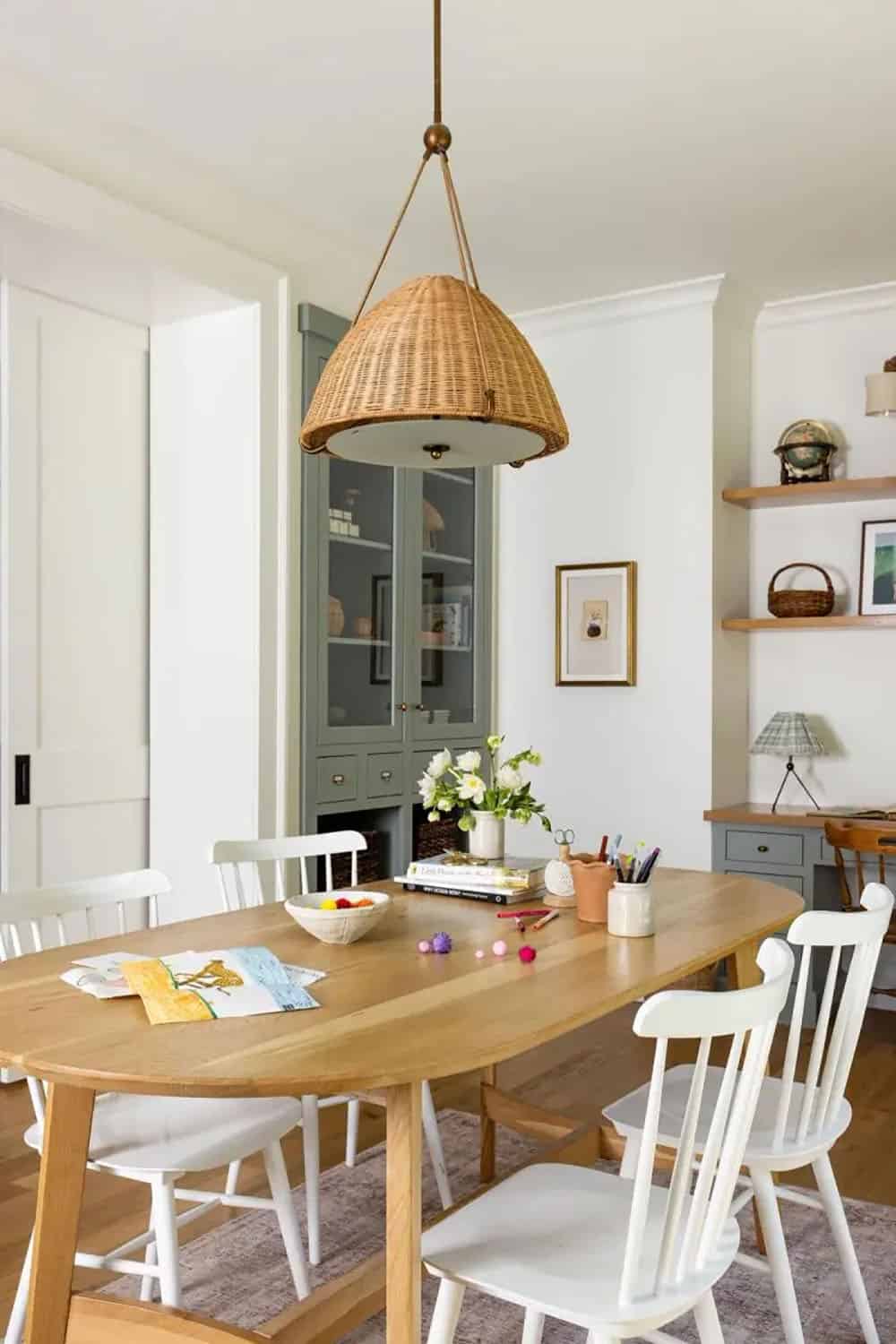 Dining room with oval table, wicker pendant light, and sage green glass-front cabinet