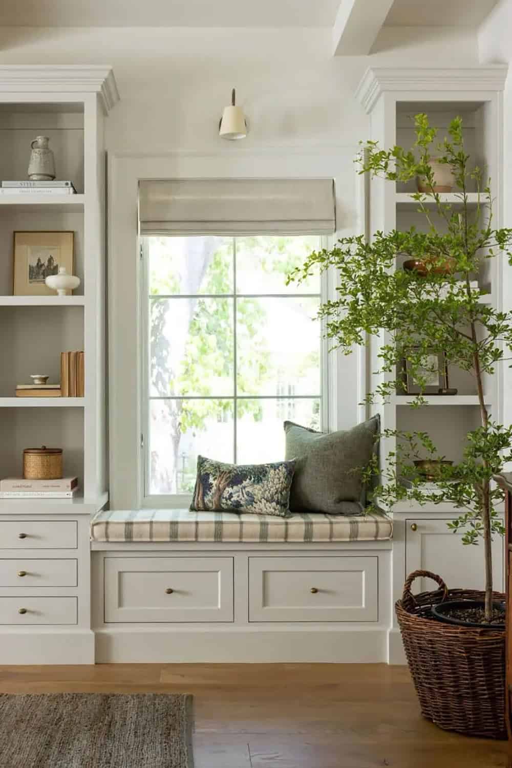Window seat with plaid cushion, flanked by built-in shelves and indoor tree