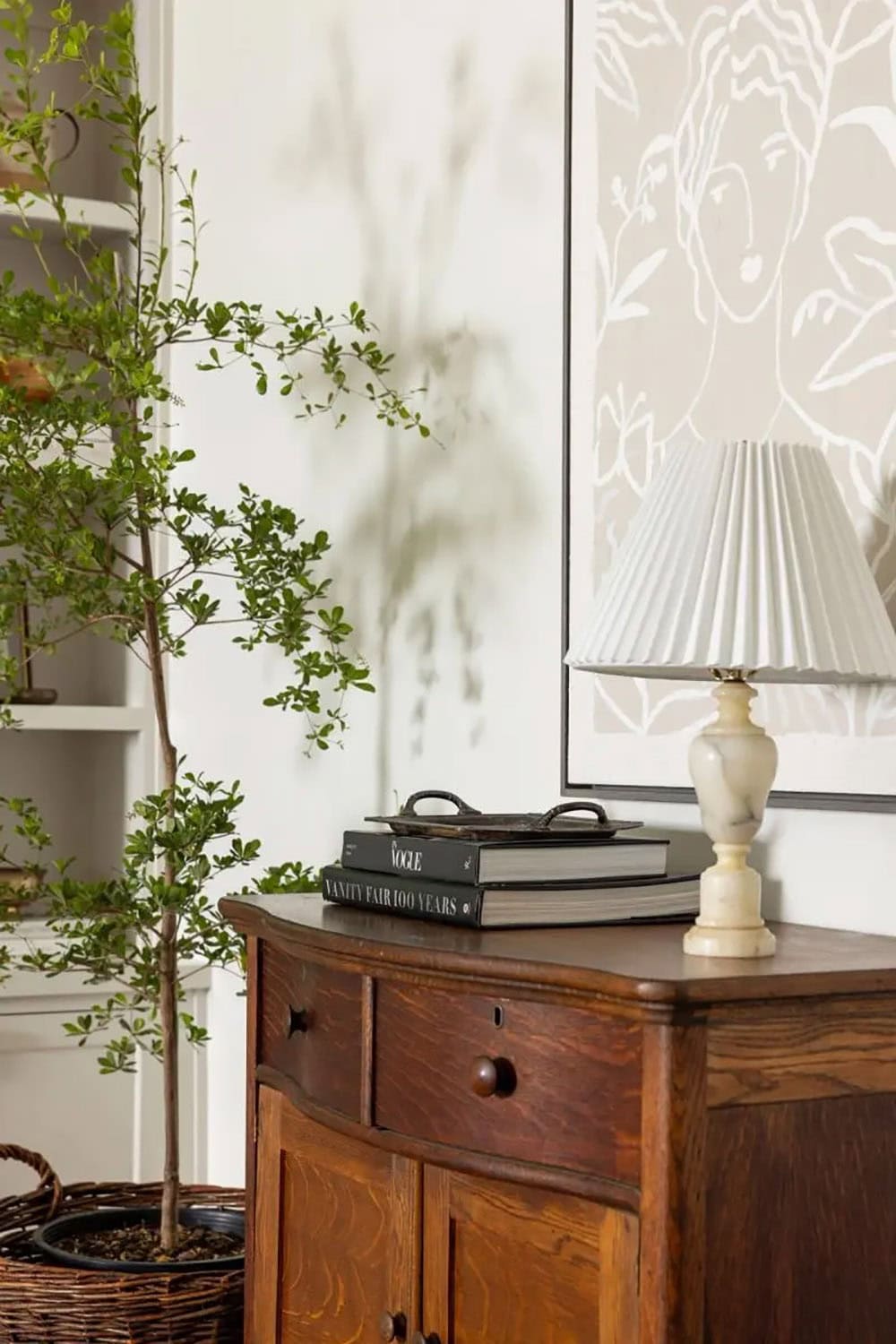 Dark wood antique dresser with marble lamp, stacked books, and botanical wallpaper