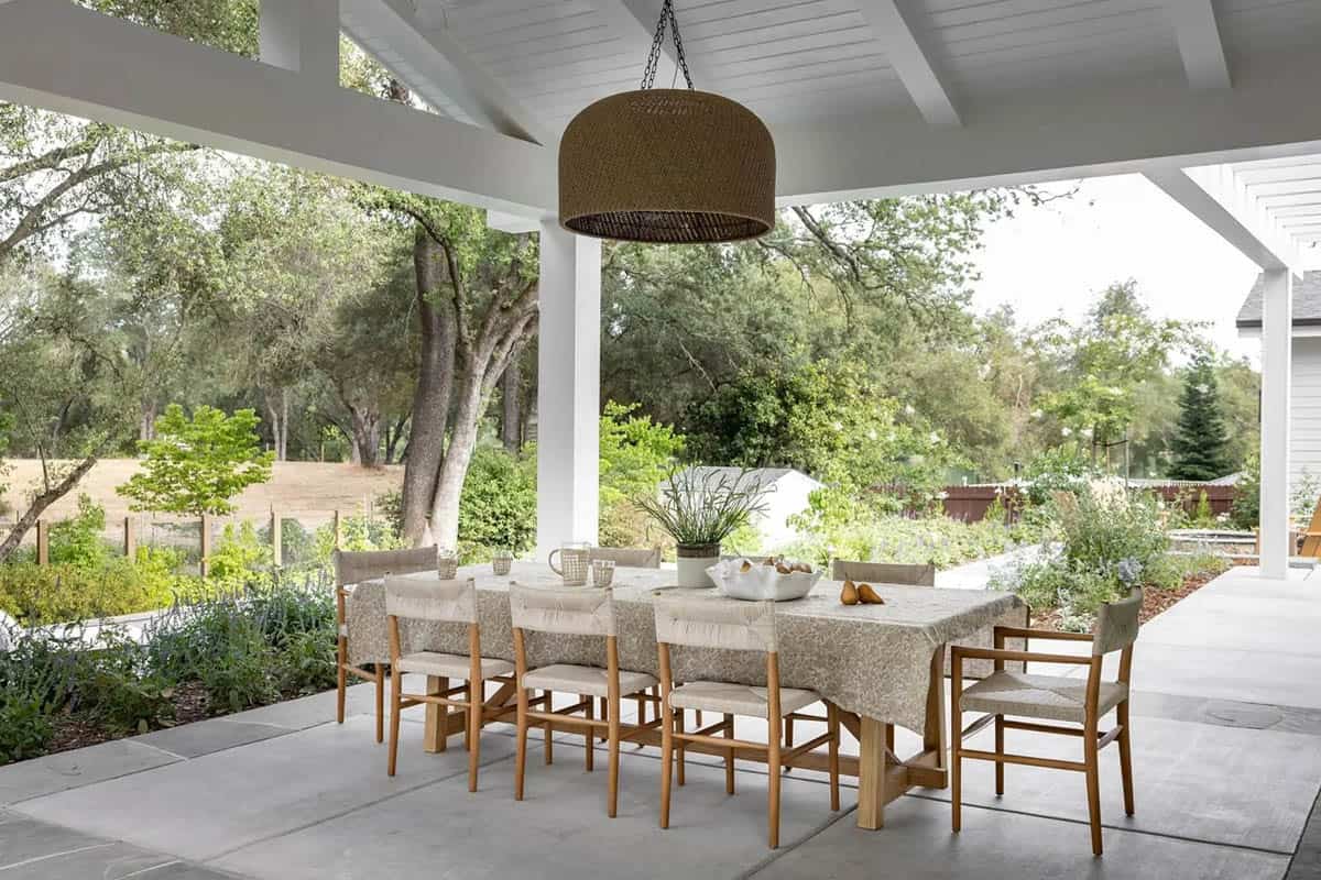 Covered outdoor dining patio with teak chairs, wicker pendant, and garden views