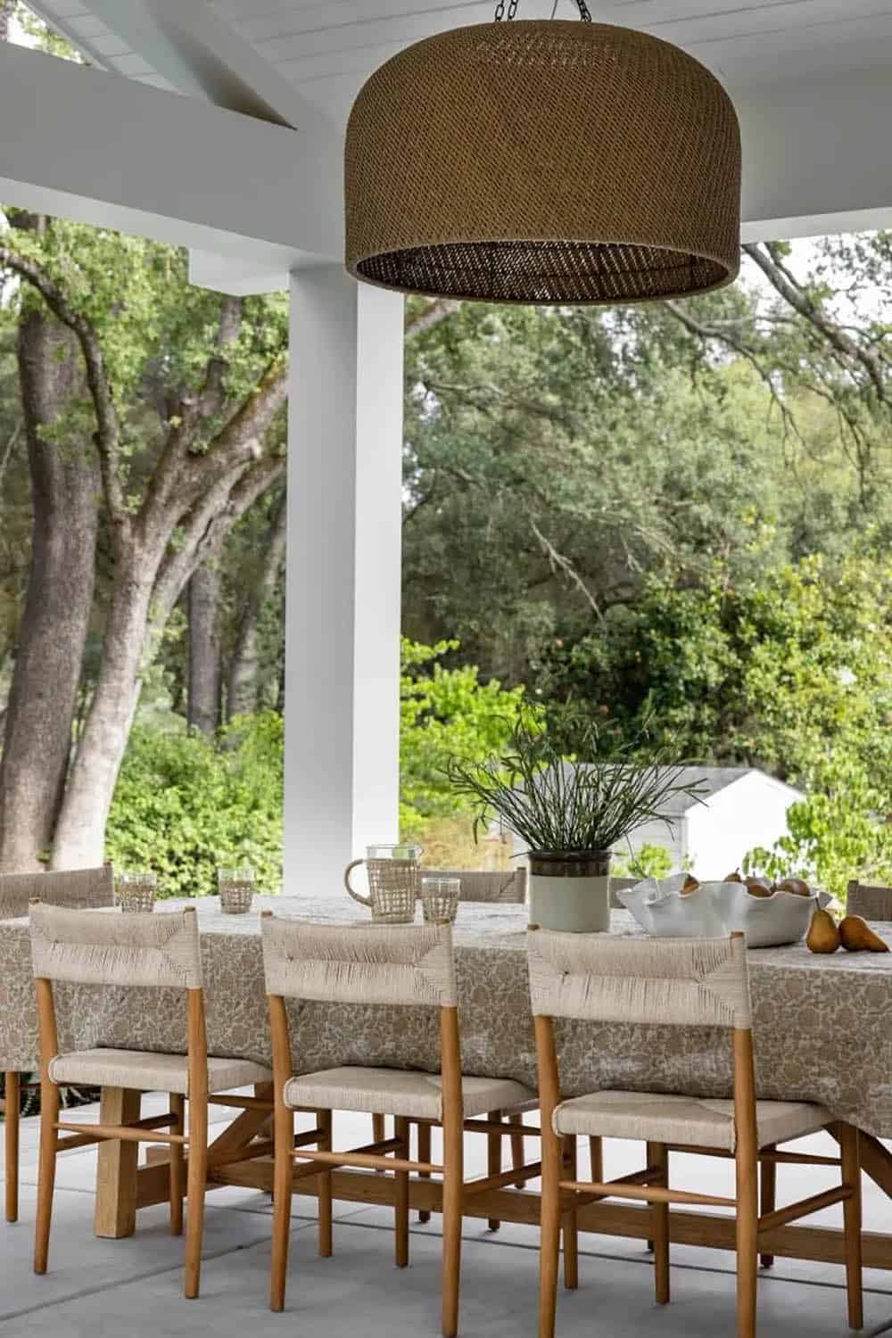 Outdoor dining table with rush-seat chairs under large wicker drum pendant