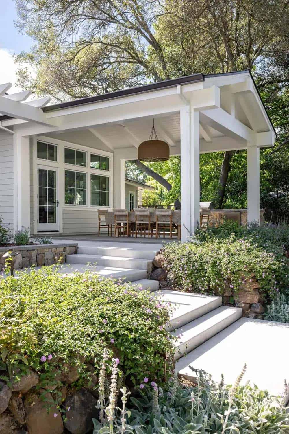 Exterior covered porch with outdoor dining set, stone steps, and lush landscaping