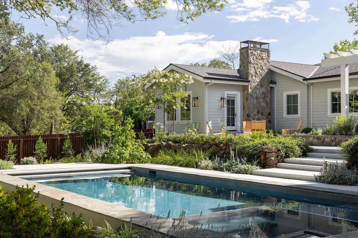 Pool and backyard with stone chimney, terraced garden beds, and mature oak trees