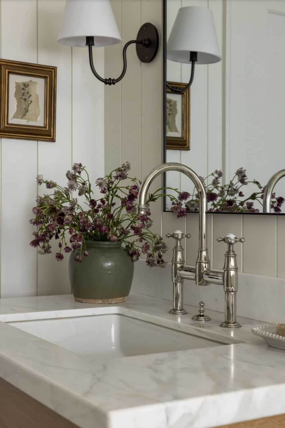 Bathroom vanity detail with bridge faucet, marble counter, and wildflower arrangement