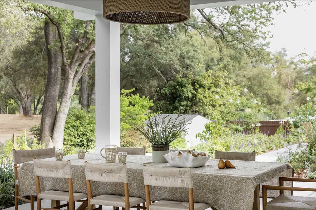 Covered outdoor dining area with floral tablecloth, rush chairs, and oak tree views