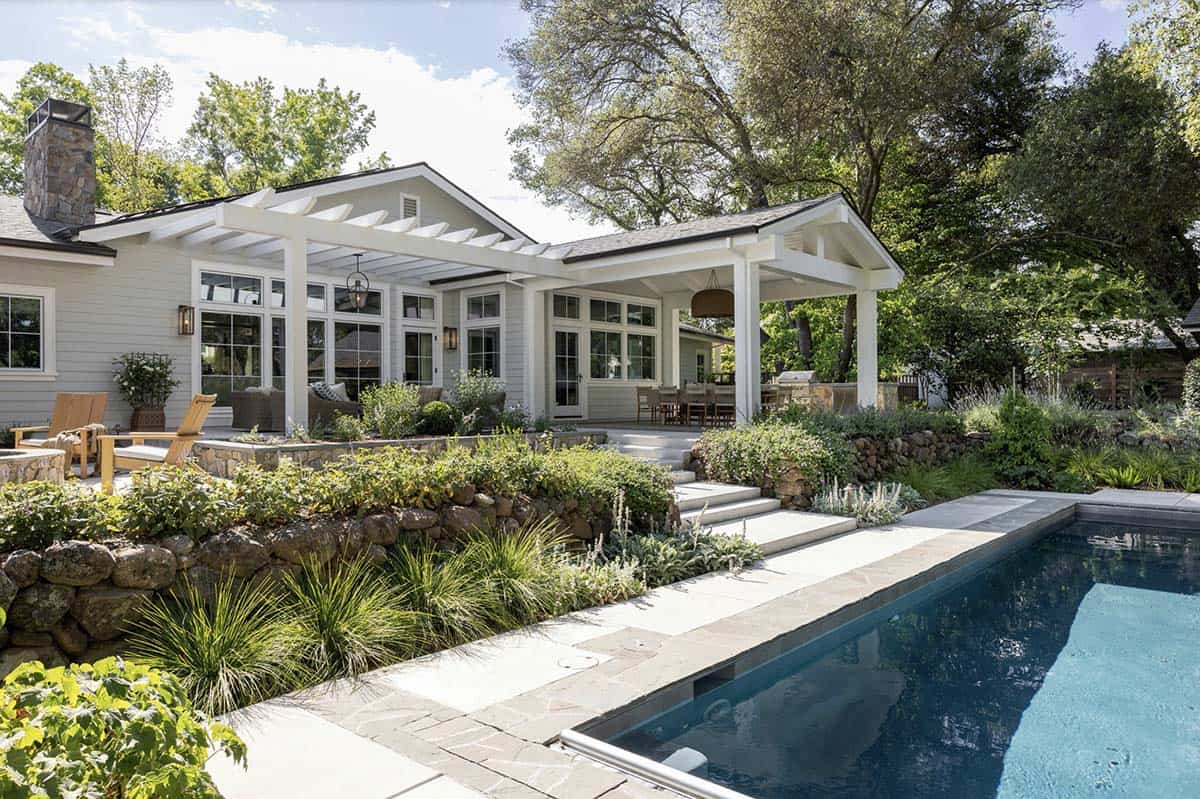 Pool and backyard view of white ranch home with covered porch and terraced landscaping