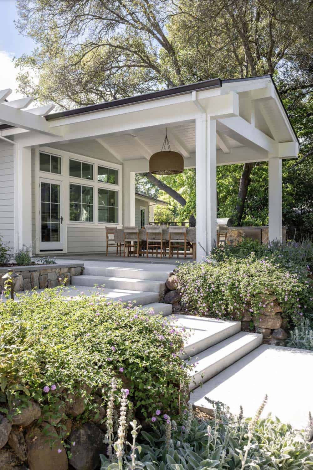 White covered patio with wicker pendant light, stone retaining wall, and garden steps