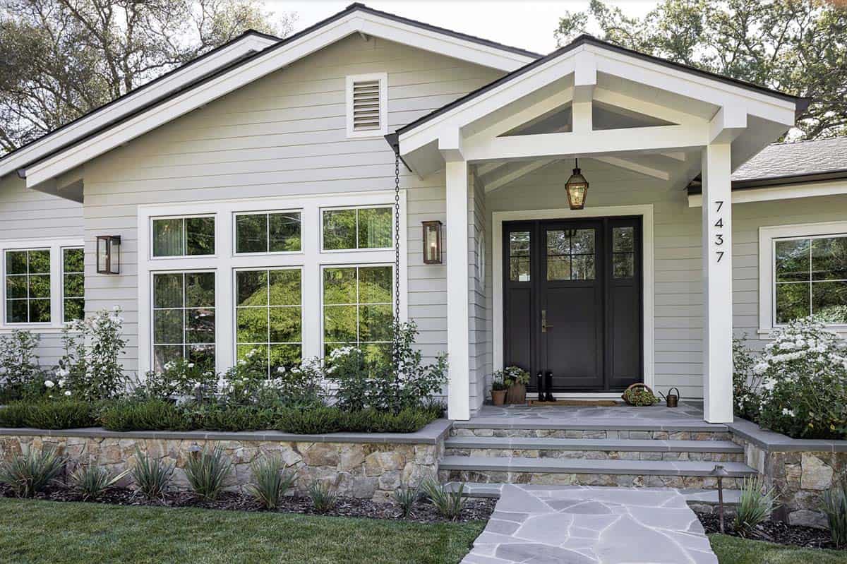 Craftsman-style home entry with black double doors, copper lanterns, and stone walkway